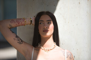 Portrait of young woman, brunette, tall, thin and very tattooed, with white top, with a lost look,...