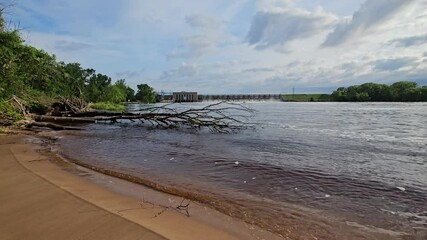 Wide angle distant view from beach at hydroelectricity dam with all spillways partially opened after heavy rains raised Wisconsin Rive level.