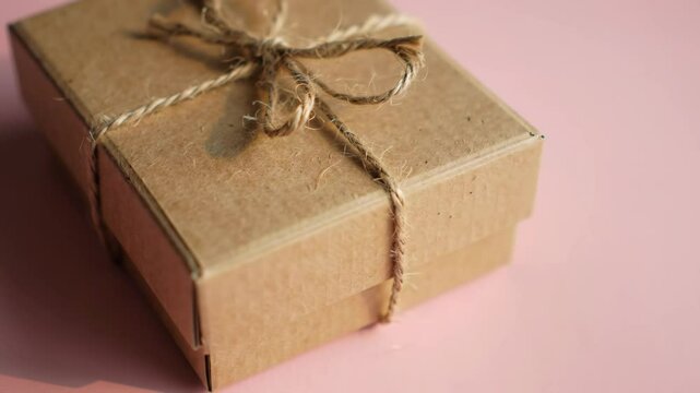 Wrapped gift box with rustic bow on a pink surface, close up