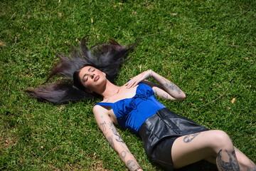 Young woman, brunette, tall, slim and very tattooed, wearing a blue top and leather shorts, with...