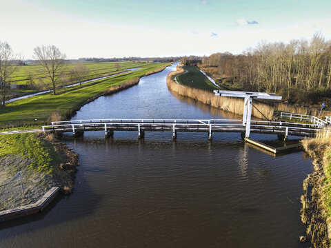 Aerial view of a serene waterway winding through the landscape, with a white bridge and lock reflecting the sky's light, Berkel en Rodenrijs, South Holland, Netherlands.