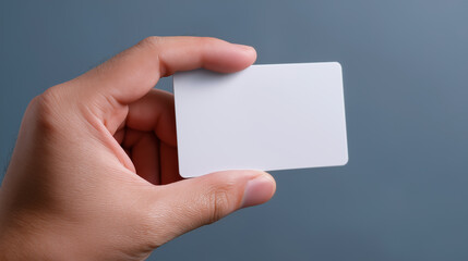 Close-up of a hand holding a blank white plastic card against a neutral background.
