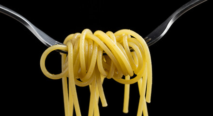 Yellow spaghetti twisted on forks against black background  
