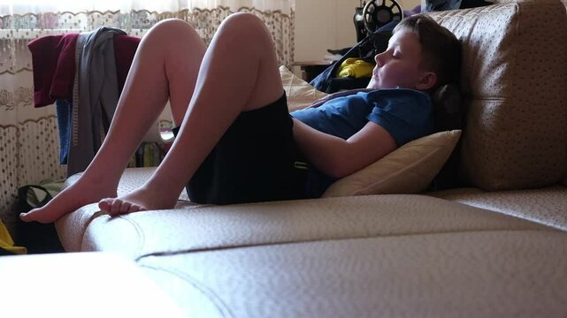 the guy is sitting on sofa and doing different things, spending time doing nothing