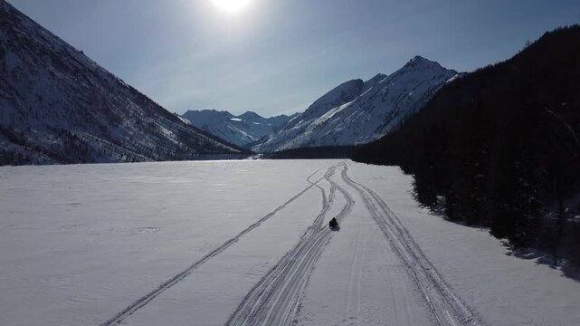 Drone aerial footage of a snowmobile riding across a frozen lake and snowy terrain in Russia. Captured from various angles, this footage highlights winter adventure, remote wilderness