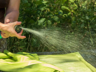 Hand holding a spray nozzle watering a vibrant green fabric outdoors