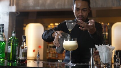 Asian bartender using strainer all ingredients alcohol liquor and syrup tasty in cocktail glass with ice serving special refresh drink showcasing nightlife mixology at luxurious nightclub. Vinosity.