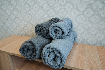 Four neatly rolled towels are skillfully arranged on a beautifully crafted wooden shelf, which adds...
