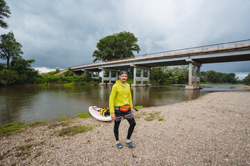 A skilled paddleboarder glides across a serene river beneath a picturesque bridge, immersed in...