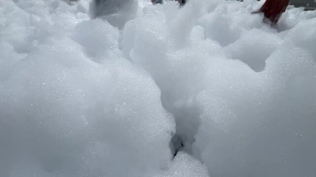 Children's feet are running on the beach in foam. White foam for a foam party. The beach is covered with a layer of foam or bubbles formed from the foam.A holiday on vacation.High quality 4k footage