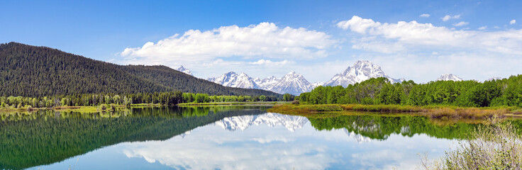 Scenic panoramic view of snow capped mountains in the Grand Teton National Park reflected in the still waters of a lake. No people.