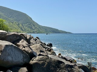 view of a rocky coast of Guadeloupe in the French West Indies with rocks and a mountain on a sunny...