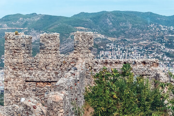 The ancient stone walls of Alanya Castle in Turkey rise against the backdrop of the town and surrounding mountains. The fortress offers a panoramic view of the Mediterranean coastline and city below