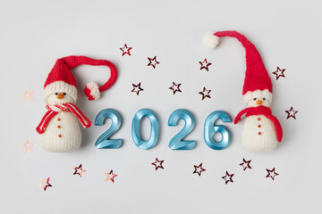 Knitted toy snowman in red hat and scarf with blue numbers 2026 and glitter stars on gray...