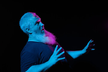 Man with a beard appears to be singing or shouting, hands in motion, with dynamic blue and pink...