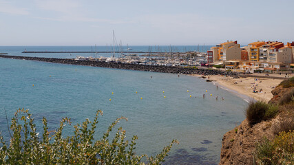 Blick auf den Hafen von Cap d&rsquo;Agde in S&uuml;dfrankreich mit einem kleinen Strand im Vordergrund und blauem Wasser.