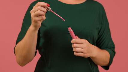 pink liquid lipstick in hands against a green dress on a pink background