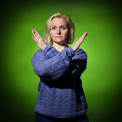 a serious woman in blue crossed her arms in front of her showing a stop sign. spot of green light on a dark background