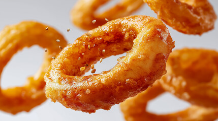 Golden crispy onion rings flying in the air with spices on white background