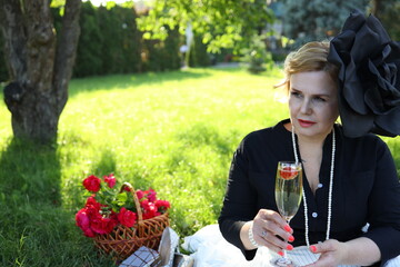 A stylish woman with a large flower accessory enjoys a refreshing drink in a vibrant garden, accompanied by a basket of fresh flowers. The atmosphere is serene and inviting.