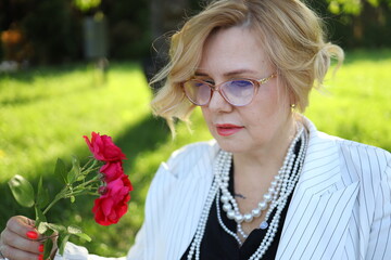 A woman dressed in a stylish striped blazer and pearls stands amidst a vibrant garden, gently...