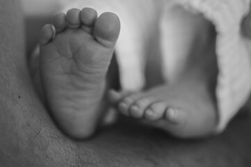A tender black and white close-up of a newborn baby's tiny feet in loving hands. Symbolizing new...