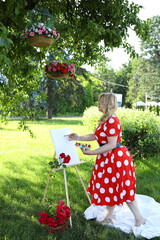 A woman in a polka dot dress stands barefoot in a garden, painting on an easel beneath a tree....