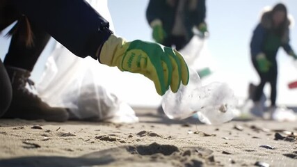 Gloved hand picking up plastic bottle during beach cleanup on sand, symbolizing environmental responsibility, pollution awareness and community efforts toward sustainability and ocean protection - Powered by Adobe