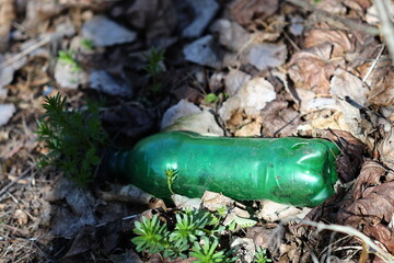 A discarded green plastic bottle lying on the grassy or sandy surface