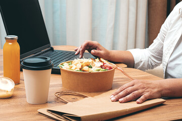 a woman is working on a laptop at home, there is food on the table, salad, coffee and juice,...