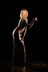 Woman in a shiny silver dress moves and dances on a black background
