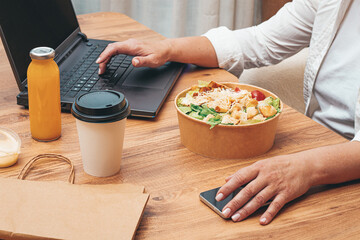 a woman is working on a laptop at home, there is food on the table, salad, coffee and juice,...