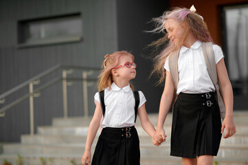 smiling schoolgirls with backpacks holding hands outdoors, wearing uniforms, emphasize friendship...