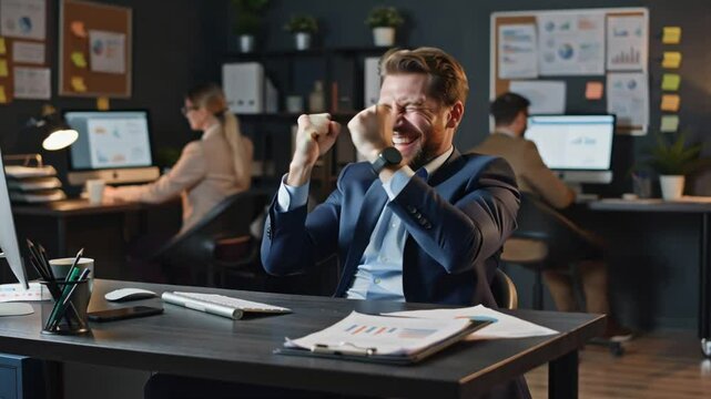 happy emotional businessman raised hands with joy in modern office sitting at table, success