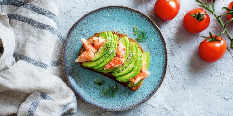 Toasted bread topped with sliced avocado, crab meat, and sprinkled with salt on a blue ceramic plate with fresh tomatoes nearby