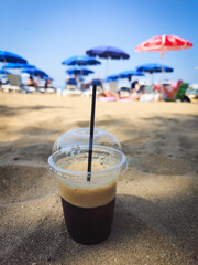 Cold refreshment iced coffee on a sandy beach. Freddo espresso refreshment at summertime.