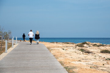 People walking on wooden pathway by the sea enjoying sunny day