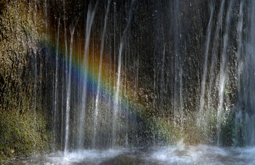 Rainbow forming on waterfall cascading down mossy rock face