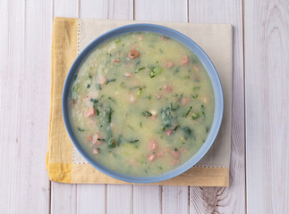 Traditional portuguese green soup with potato, green cabbage and sausage over wooden table