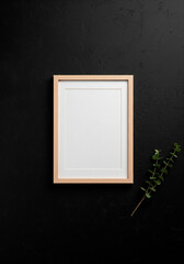 Blank wooden frame mockup with green branch on black background for art prints, branding or minimalist interior visuals