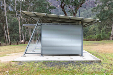 Photograph of a reasonably well maintained steel and corrugated iron unisex toilet block on a concrete base located in a large public use campground facility.
