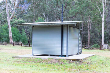Photograph of a reasonably well maintained steel and corrugated iron unisex toilet block on a concrete base located in a large public use campground facility.
