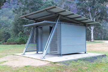 Photograph of a reasonably well maintained steel and corrugated iron unisex toilet block on a concrete base located in a large public use campground facility.