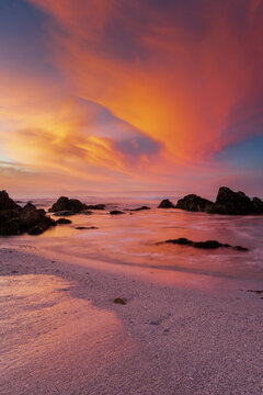 View of a serene seascape with rocks scattered along the shoreline and a vivid sunset painting the sky with warm hues, Hermanus, Western Cape, South Africa.