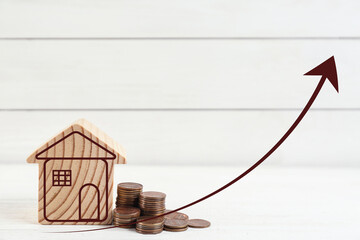 Increase in real estate value. House model and coins on table. Growing price represented by arrow