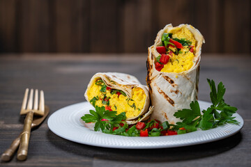 Homemade healthy trendy breakfast eggs burrito with vegetables and herbs in white plate on wooden...