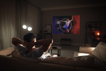 Man watching sports event using video projector on sofa at night