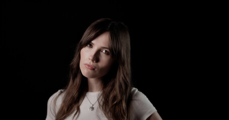 Studio portrait of a young woman with long brown hair and white t shirt expressing seriousness...