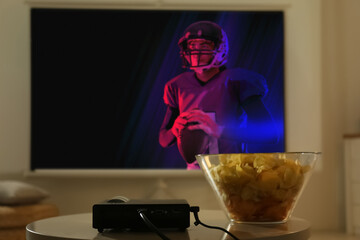 Video projector and bowl with chips on wooden table. Ready to watch sports event