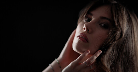 Young woman gently touching her face and neck with hands on dark background